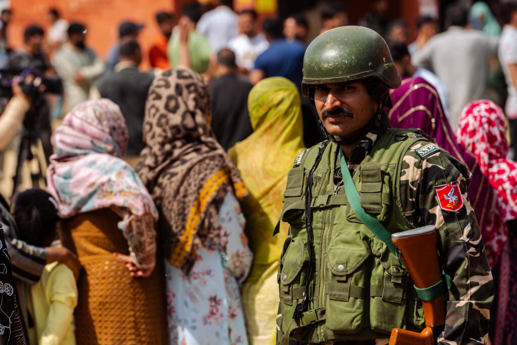 Un soldato in Kashmir presidia i seggi. Sullo sfondo una fila di donne in attesa di votare.