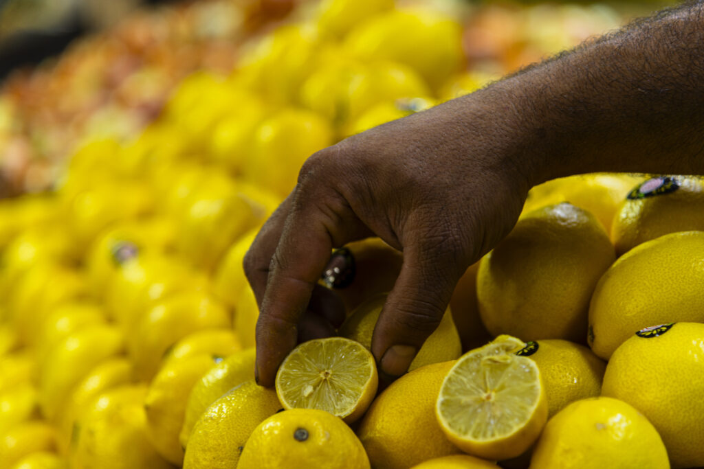 Ramallah Palestine - A colorful stand of lemons. Some lemons are cut. A vendor's hand turns a cut half lemon toward the room.