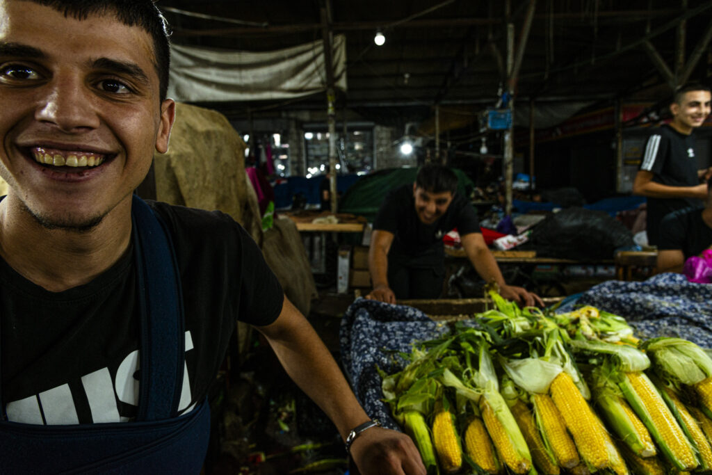 Ramallah, Palestine - Marketplace - young corn vendors laugh in amusement at being caught by my camera. One young man is in the foreground, the second leans against the maize counter as he laughs.