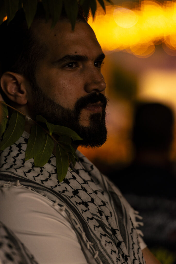 Ramallah, Palestina - Fotografia notturna di un giovane uomo palestinese indossa una Keffiyeh attorno al collo e sulle spalle, intento a guardare uno spettacolo di danze e musiche popolari