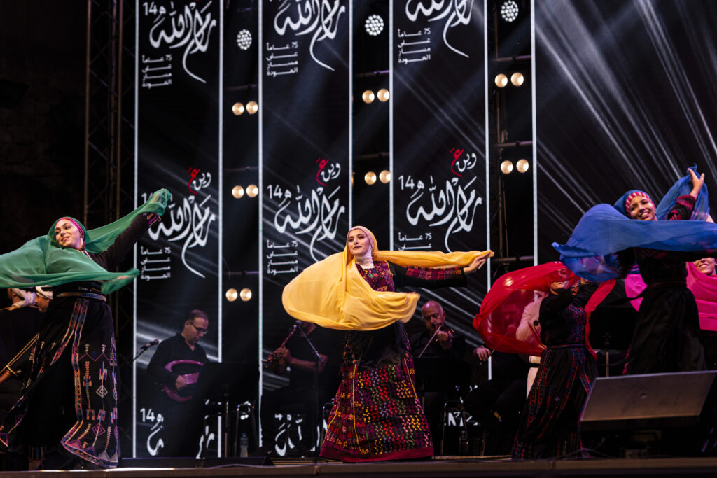 Ramallah, Palestine - A group of young female dancers perform on a stage where traditional Palestinian folk music is played. The dancers wear colorful clothes and twirl the veils with which they cover their heads and shoulders.