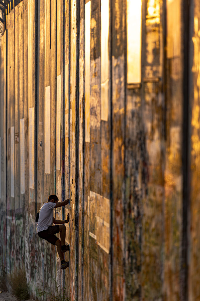 Il muro di separazione a Betlemme è uno dei luoghi più visitati da parte di chi vuole conoscere gli effetti dell'apartheid israeliana nei confronti dei palestinesi. Il muro, fotografato di taglio riflette la luce del tramonto, mentre un ragazzo vi si arrampica lungo una delle fessure che separa le lunghe lastre di cemento armato che lo compongono.