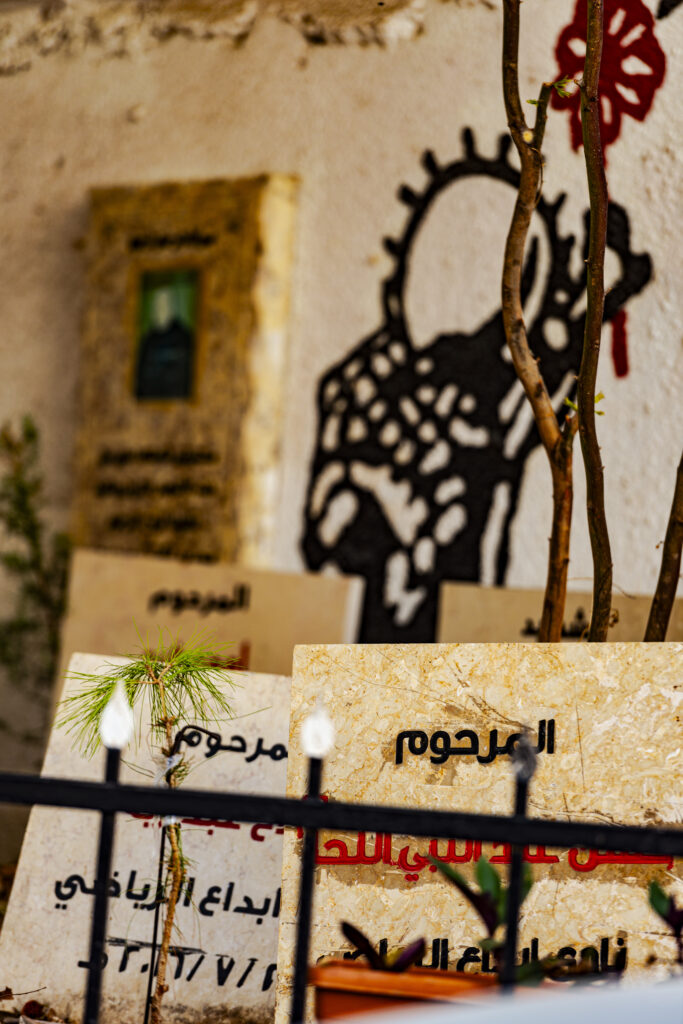 Some gravestones at the entrance to the Bethlehem refugee camp commemorate the Palestinian martyrs killed by the Israeli army. Many of them died in Israeli prisons and their bodies were not returned to their families until they had completed their sentences. An act of collective punishment that deprives the families and the martyr of the dignity of a burial. In the background you can see a drawing of Handala holding a flower in his hand. Handala is one of the symbols of the suffering of the Palestinian people. A child depicted from behind, dressed in rags, sometimes depicted with a keffiyeh, sometimes holding the key to a Palestinian house, sometimes with a raised fist, sometimes with a weapon. more often with his hands behind his back, as a sign of resignation. Handala is a character by the illustrator Naji al-Ali, assassinated in London in 1987, probably by Mossad agents. Here Handala is depicted with a red flower in his hand and a keffiyeh on his shoulders.