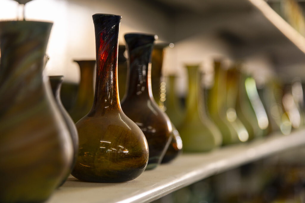 Delle ampolle di vetro, di colore rosso e di colore verde sono appoggiate su una mensola bianca in uno degli scaffali del negozio adiacente al laboratorio.