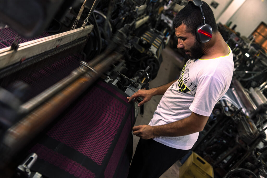 The last Kufiyah factory in Palestine's Hebron. A young craftsman is pictured working at the loom on a purple Kufiyah. He wears headphones to protect his ears from the noise of the incessantly working machines.