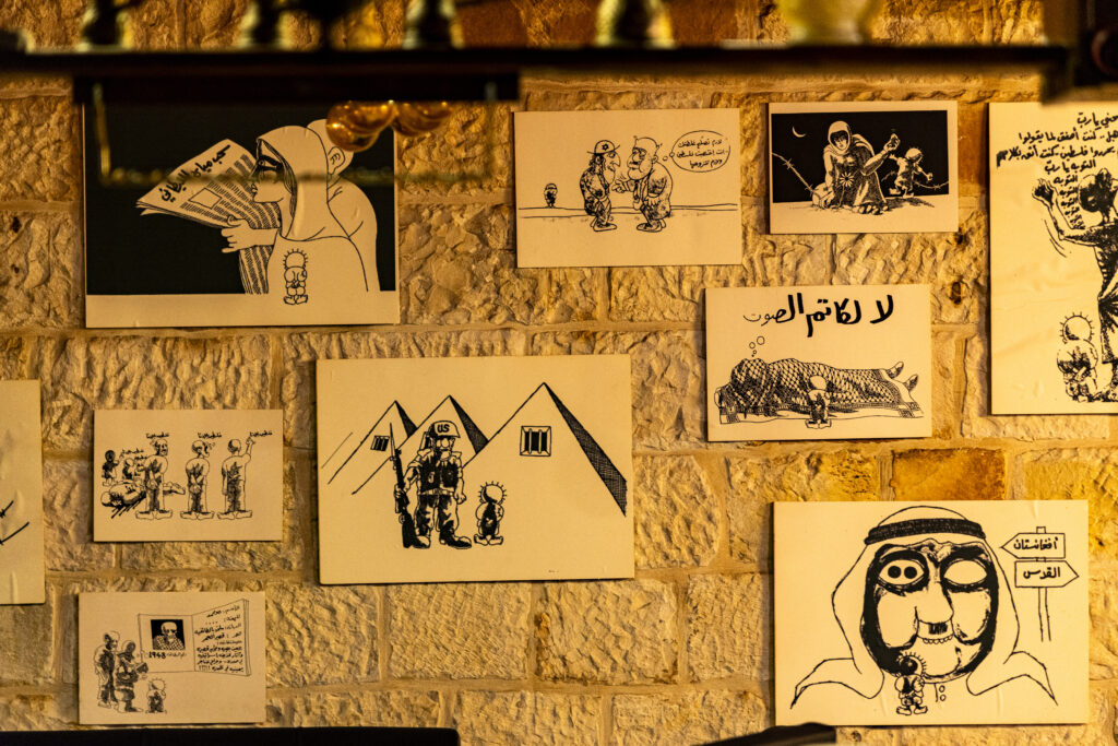 A wall of the Handala Café covered with reproductions of Naji al-Ali's illustrations. The photo was taken in the darkness of the café, which was closed at the time of the visit.