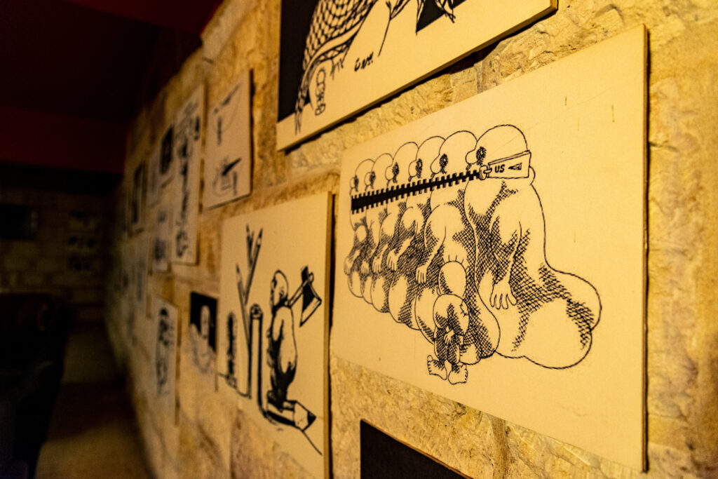A wall of the Handala Café, photographed in slash, covered with reproductions of Naji al-Ali's illustrations. The photo is taken in the darkness of the café, which was closed at the time of the visit.