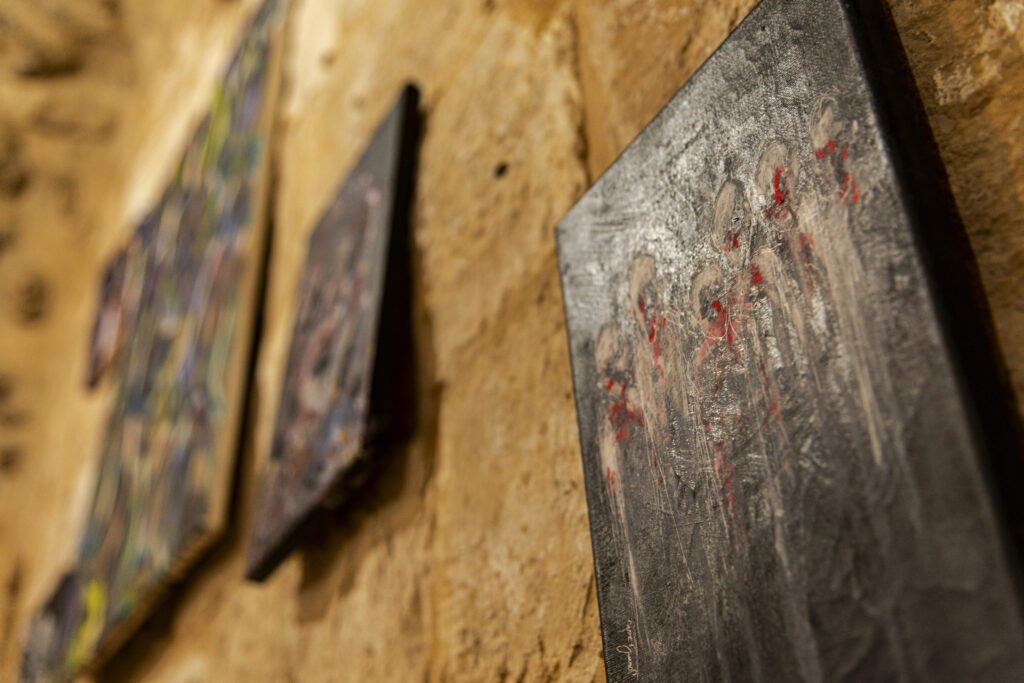 A wall with three paintings taken from below. The three paintings partly reflect the light. They are dark on a white rock wall.