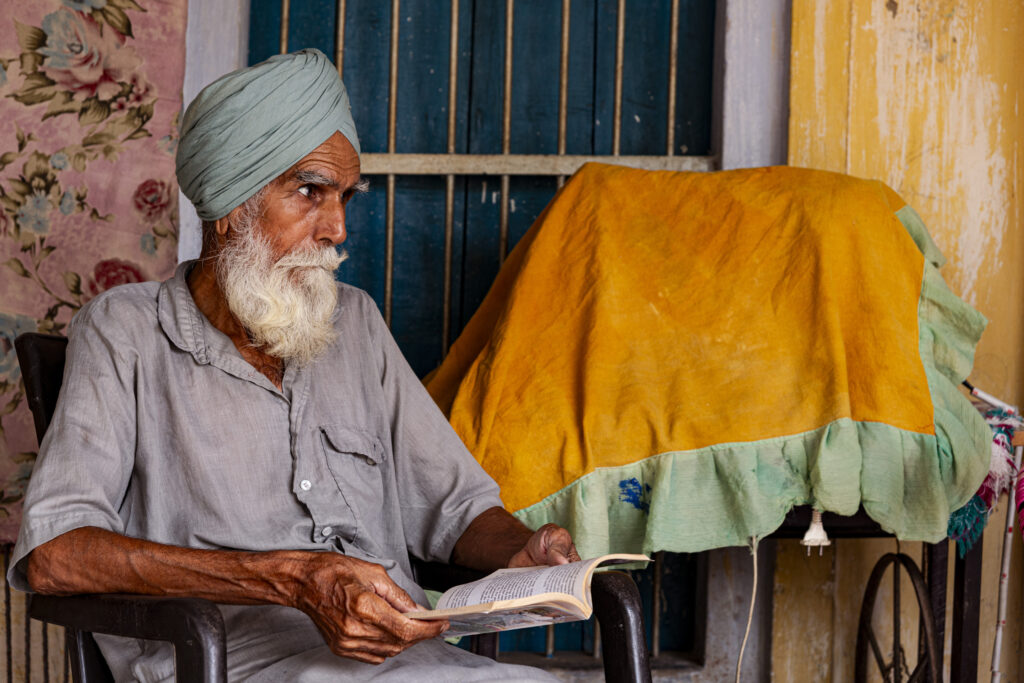 Swarn singh di Karamgarh Sattran del distretto di Bathinda. Un uomo in età avanzata vestito con una Kurtha grigia e un turbante azzurro, nel cortile della sua casa legge un libro sull'agricoltura biologica.