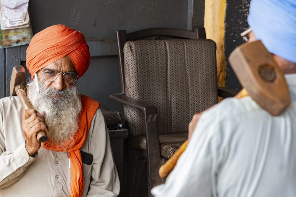 In a carpentry workshop in Jaitu, two craftsmen work together with their hammers to shape various tools and iron parts.