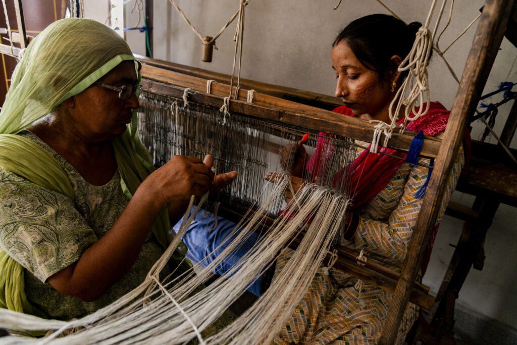 The weaving teacher and one of the students prepare a loom for weaving. Preparing a loom involves several hours of work.